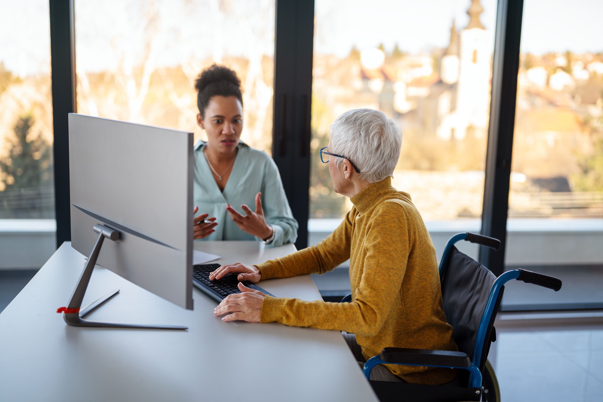 Business woman in wheelchair working with colleague in modern inclusive office. Diversity, support